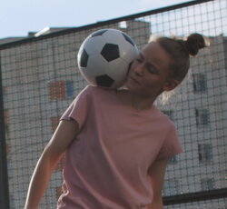 A girl holding a soccer ball on her shoulder